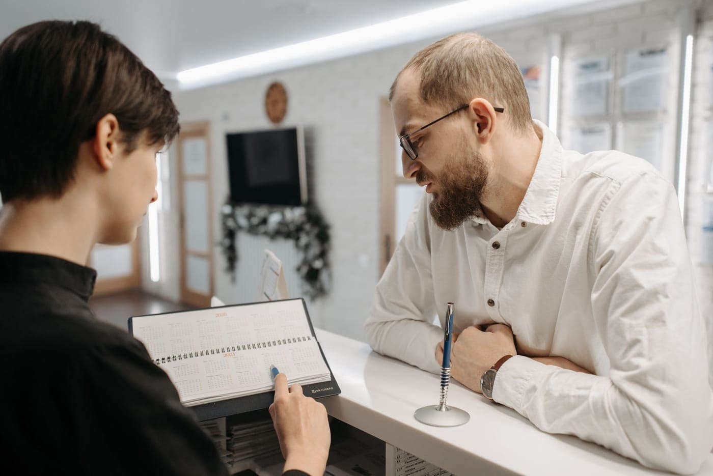 Una recepcionista revisa la agenda con un cliente en el mostrador